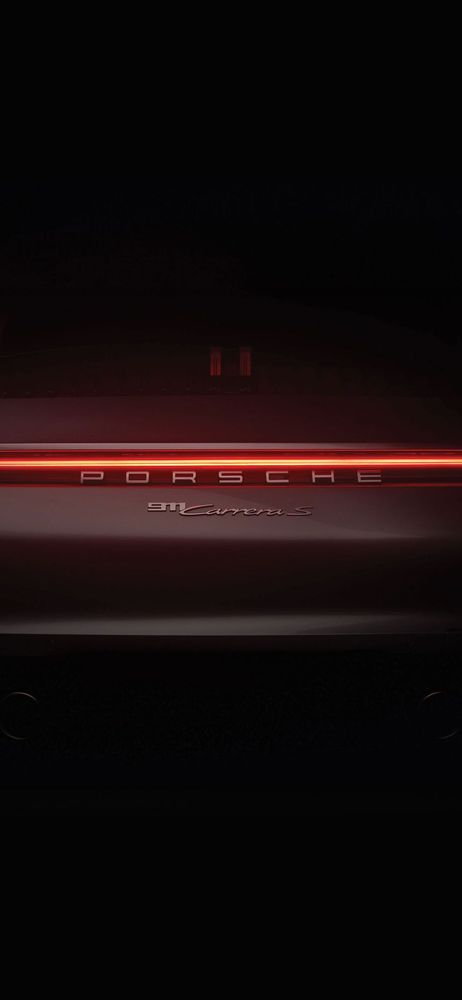 Rear view of a Porsche car in the dark with its illuminated red LED taillight strip.